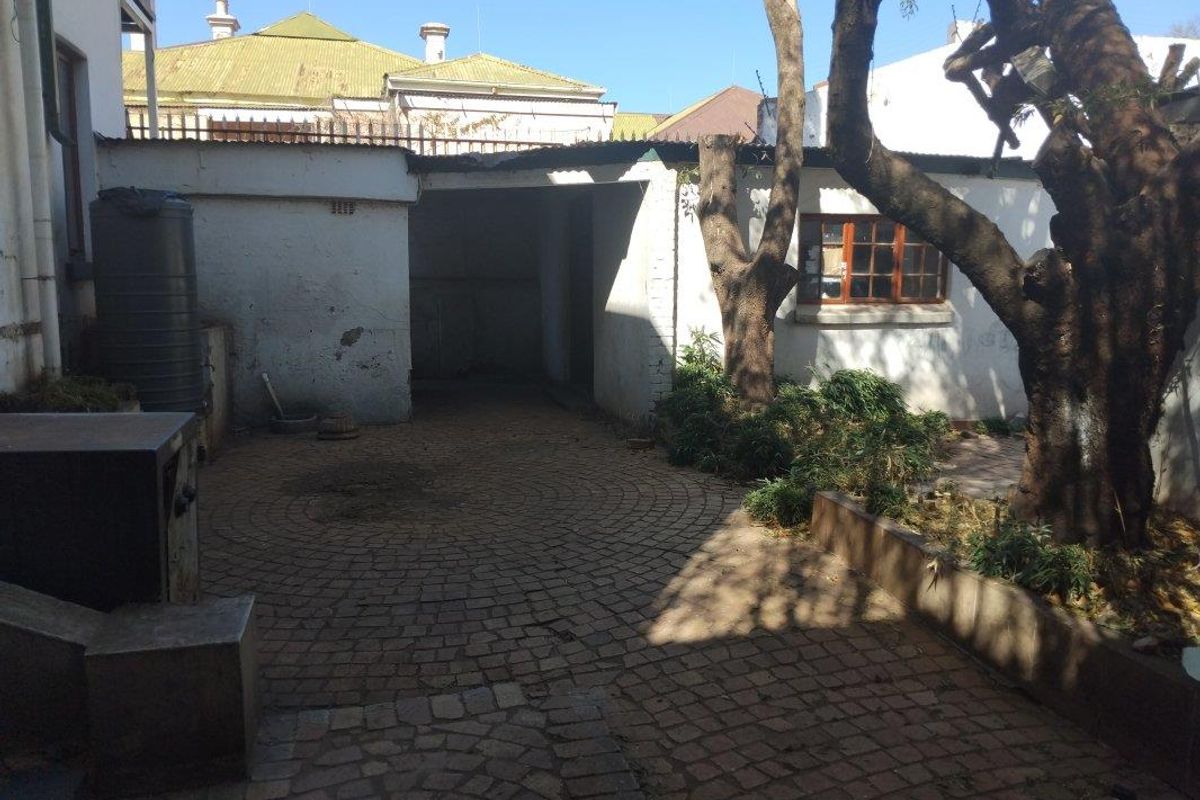 A rear courtyard area featuring paved flooring, a water tank, and mature trees, requiring maintenance to the exterior wall finishes.