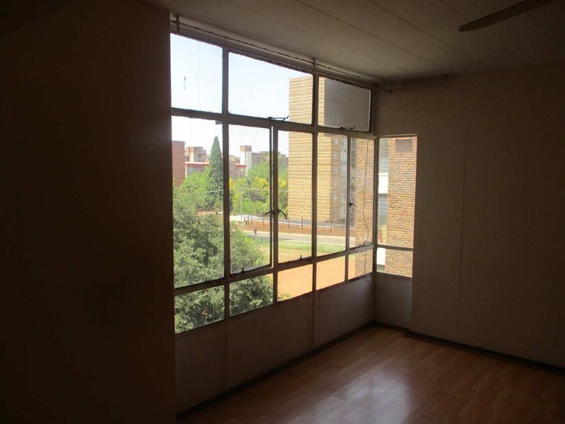 An empty living room featuring large steel-framed windows that provide ample natural light and views of the surrounding neighborhood.