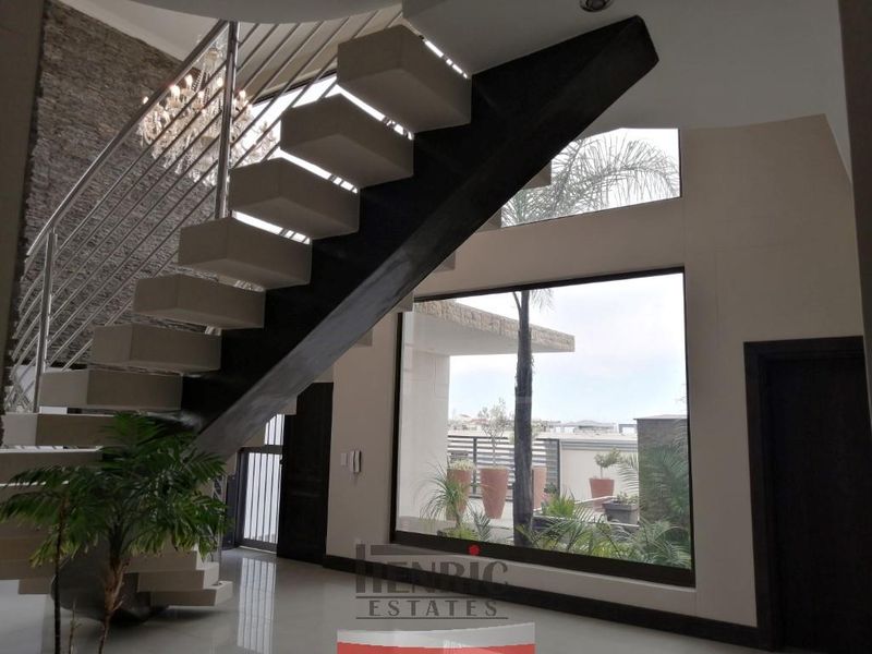Modern entrance hall featuring a striking floating staircase with stainless steel balustrades, large picture windows, and a textured stone feature wall.