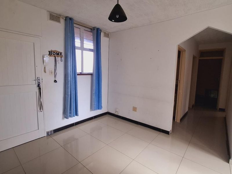 An empty living area featuring tiled flooring, an intercom system, and a distinctive archway leading to the hallway.