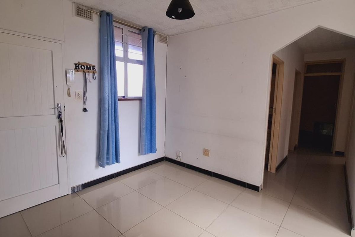 An empty living area featuring tiled flooring, an intercom system, and a distinctive archway leading to the hallway.