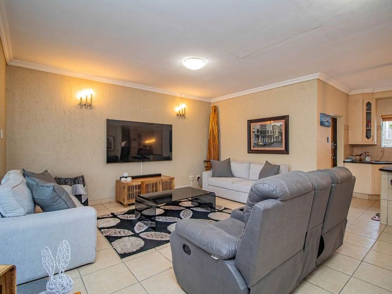 Open-plan living area featuring tiled flooring, coved cornicing, and a connected kitchen space with cabinetry and a breakfast bar.