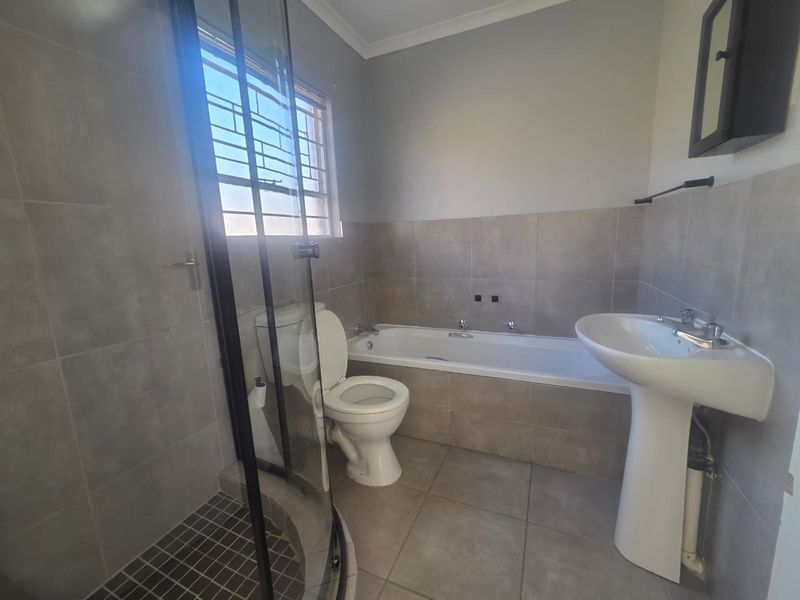 A functional bathroom featuring a shower enclosure, bathtub, pedestal basin, and toilet with neutral wall and floor tiling.