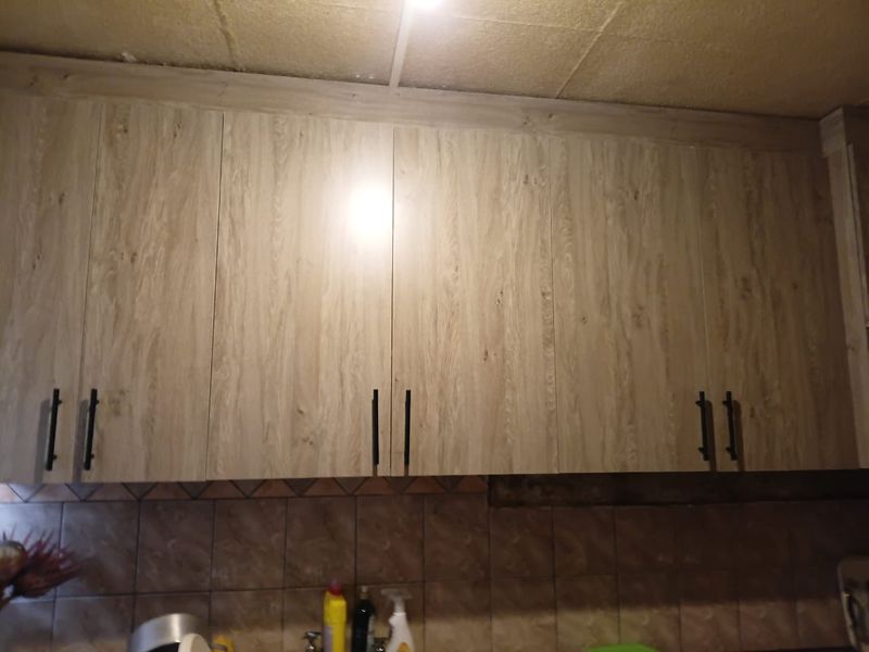 Close-up view of kitchen wall cabinetry with wood-look finish, tiled backsplash, and visible ceiling and wall damage requiring maintenance.