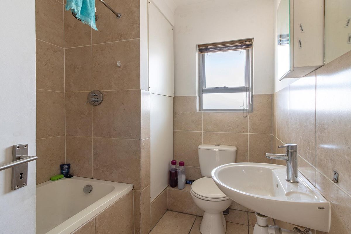 A functional bathroom featuring a bathtub with shower mixer, pedestal basin, and toilet, finished with neutral wall and floor tiling.