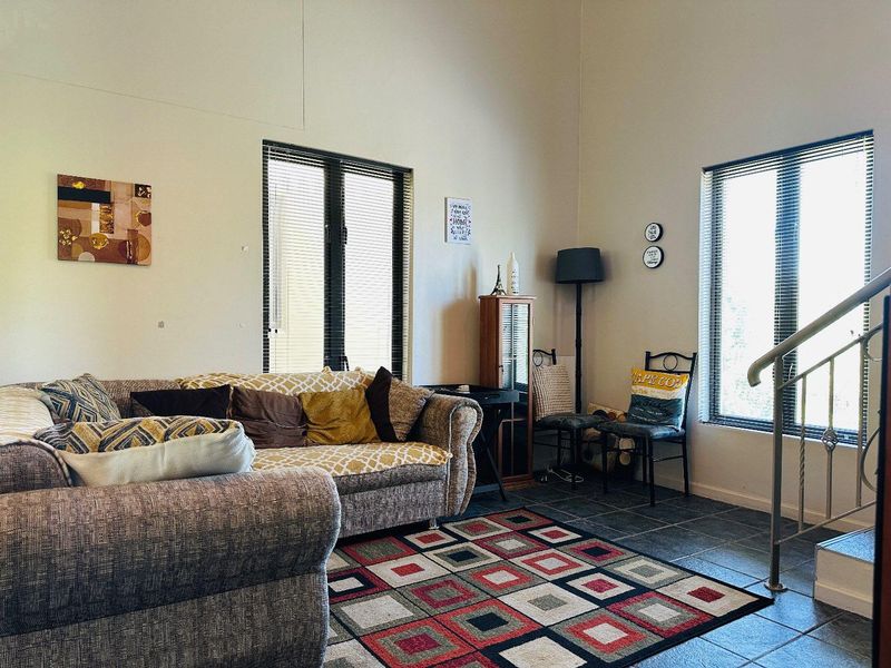 A living room featuring tiled flooring, large windows with venetian blinds, and a staircase railing, offering a bright and functional living space.