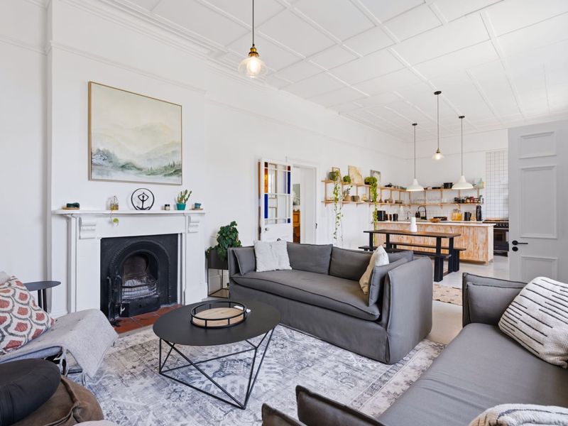 Spacious open-plan living and kitchen area featuring a classic fireplace, coffered ceilings, and a functional kitchen island with open shelving.