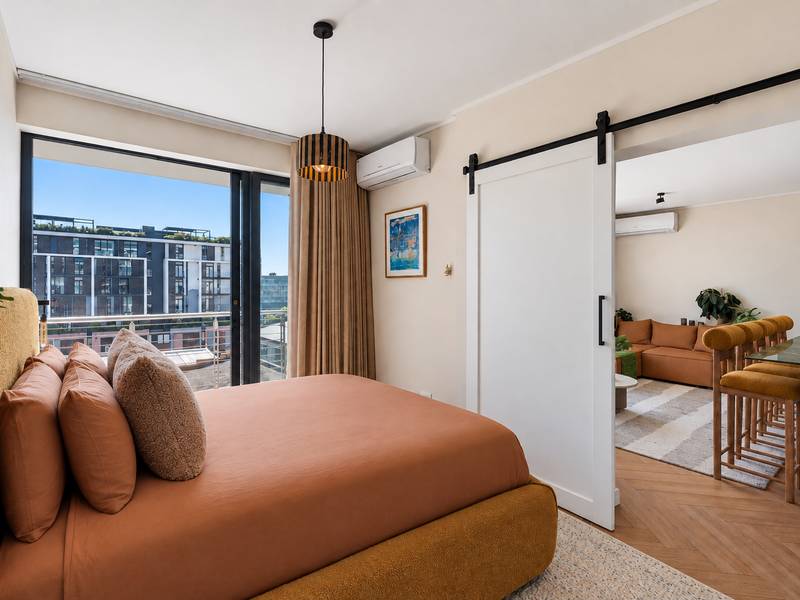 A well-appointed bedroom featuring herringbone timber flooring, a modern sliding barn door, split-system air conditioning, and large windows with urban views.