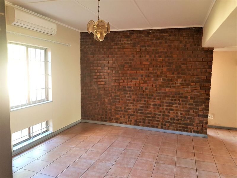 A spacious living area featuring a prominent exposed brick feature wall, tiled flooring, and a wall-mounted air conditioning unit.
