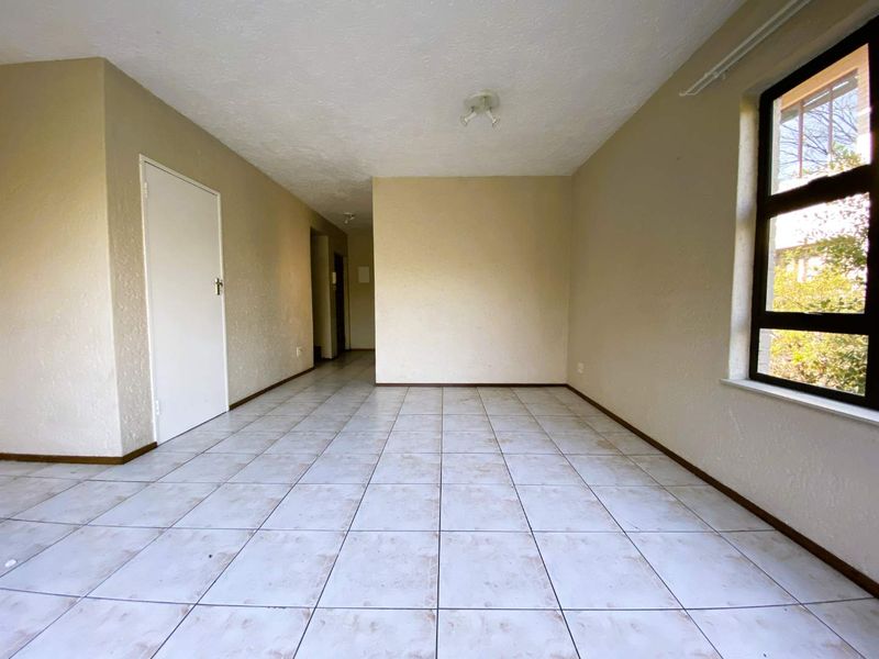 An empty, open-plan living area featuring neutral wall finishes, ceramic tiled flooring, and a large window providing natural light.