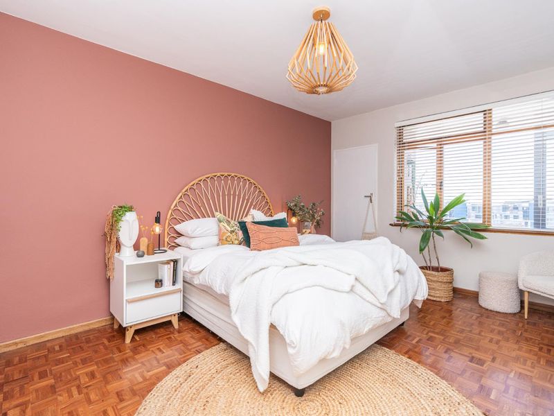 A well-maintained bedroom featuring warm parquet flooring, a feature accent wall, and natural light filtered through venetian blinds.