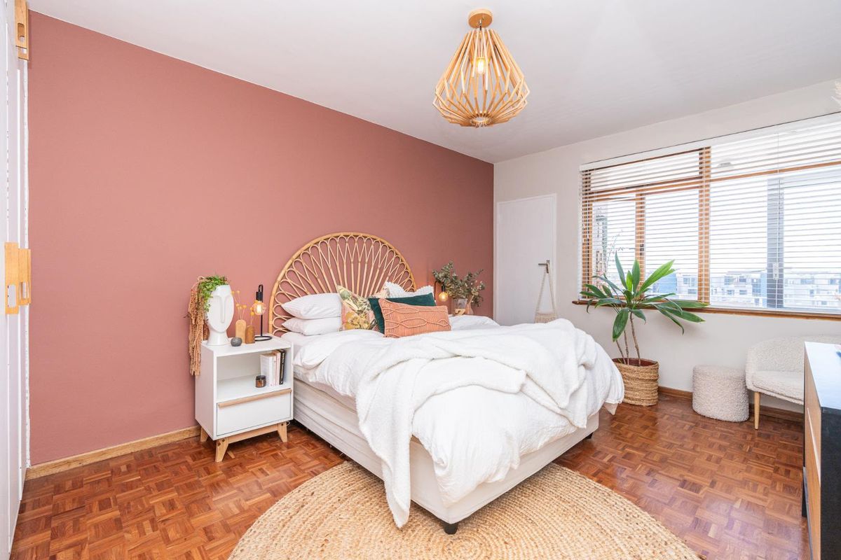 A well-maintained bedroom featuring warm parquet flooring, a feature accent wall, and natural light filtered through venetian blinds.