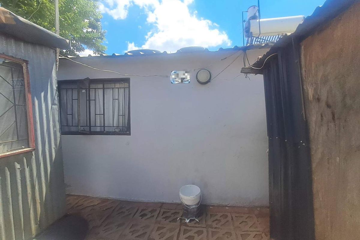 Rear exterior area featuring a paved courtyard, security-barred window, and a solar water heater mounted on the roof structure.