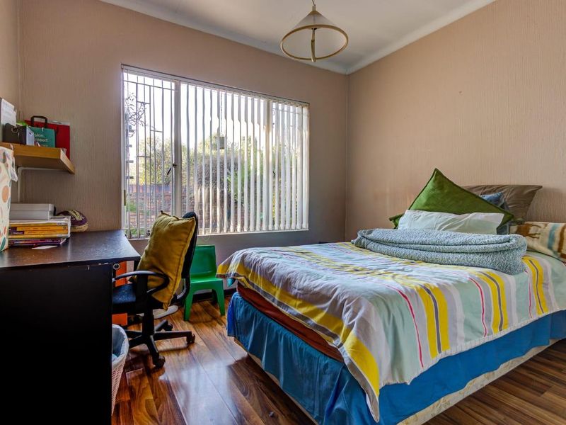 A functional bedroom featuring laminate flooring, vertical blinds, and security bars on the window, providing a comfortable and practical living space.