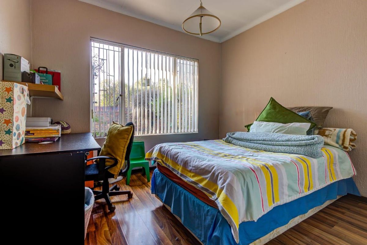 A functional bedroom featuring laminate flooring, vertical blinds, and security bars on the window, providing a comfortable and practical living space.