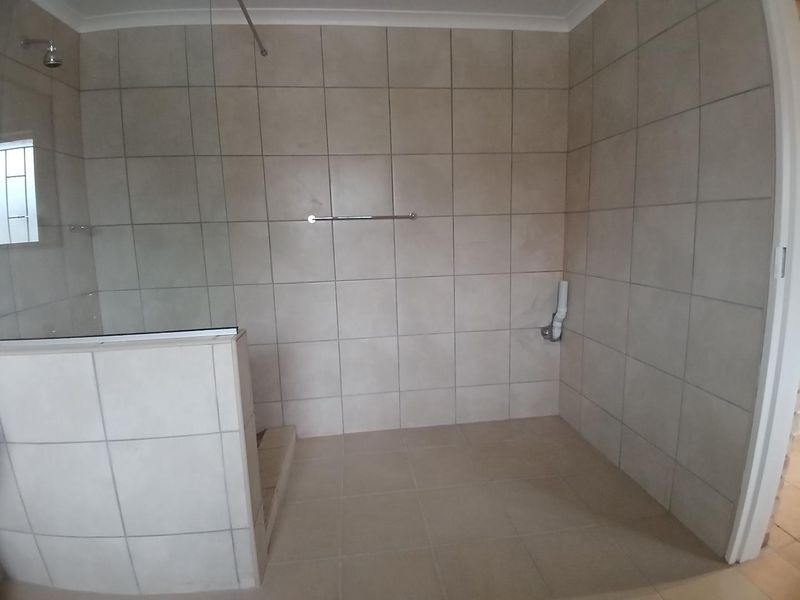 A functional bathroom featuring a walk-in shower with a glass screen and neutral ceramic tiling throughout.