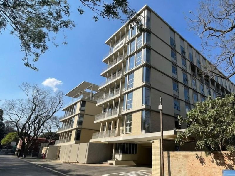 A modern multi-story apartment building featuring a contemporary facade with glass balconies and large windows, situated on a paved street.