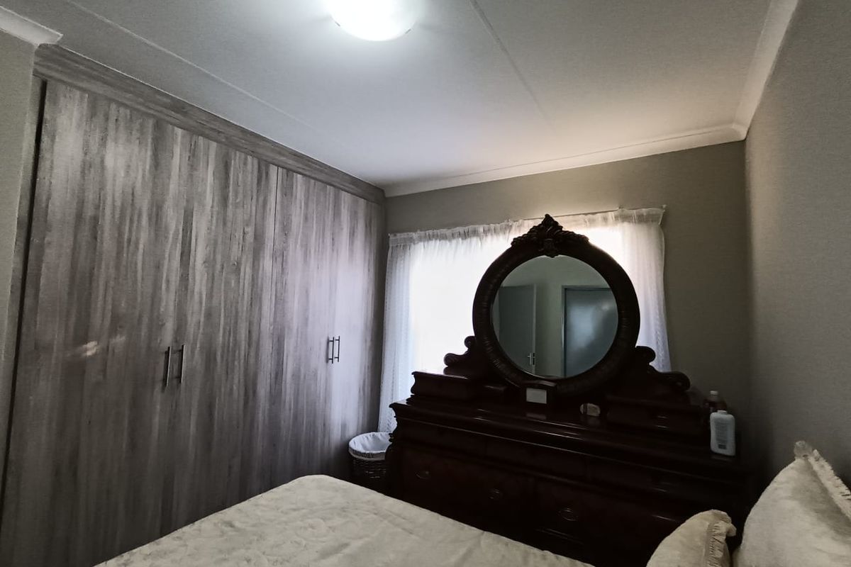 A well-maintained bedroom featuring floor-to-ceiling built-in cupboards with a wood-grain finish and decorative cove cornicing.