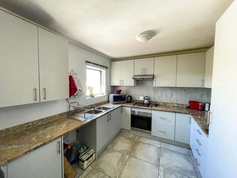 A functional kitchen featuring light-toned cabinetry, granite countertops, a double basin sink, and built-in cooking appliances with tiled flooring and backsplash.