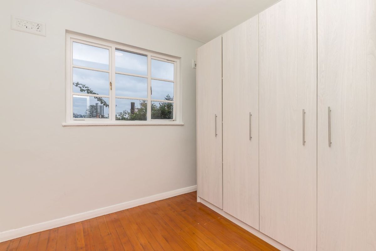 A bright, empty bedroom featuring polished timber flooring, neutral walls, and extensive built-in storage cupboards.