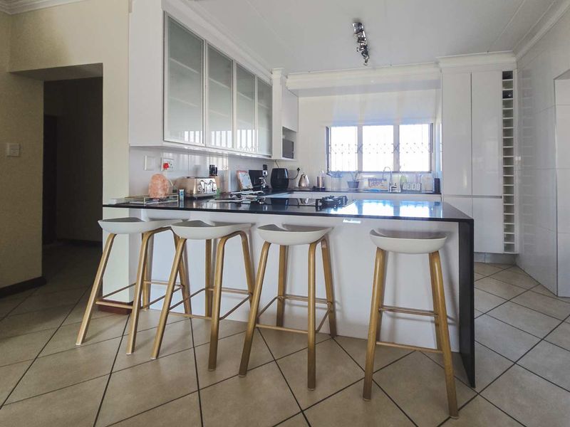 Modern kitchen featuring a central island with a stone countertop, ample built-in cabinetry, integrated appliances, and tiled flooring.