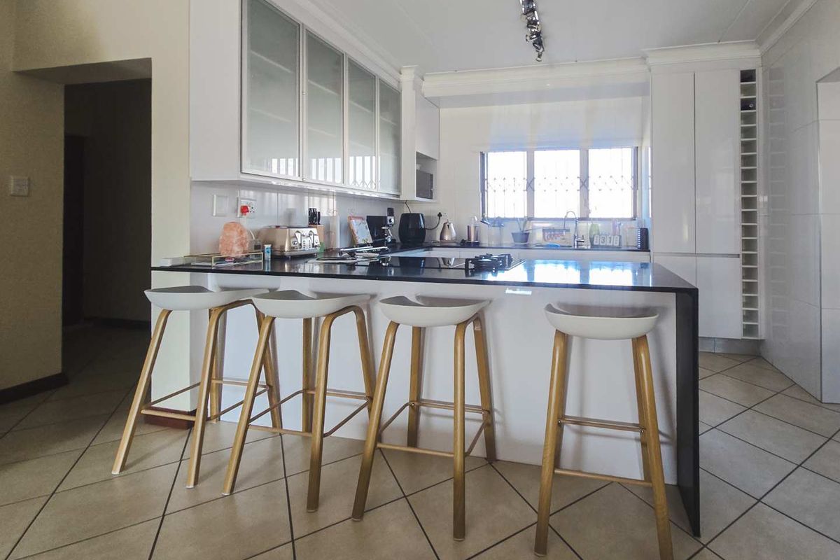 Modern kitchen featuring a central island with a stone countertop, ample built-in cabinetry, integrated appliances, and tiled flooring.