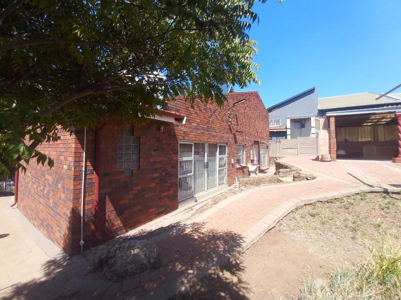 Rear view of the face brick house featuring a paved walkway, security gates, and established garden area.