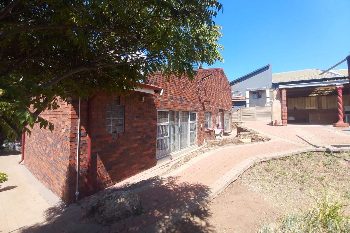 Rear view of the face brick house featuring a paved walkway, security gates, and established garden area.
