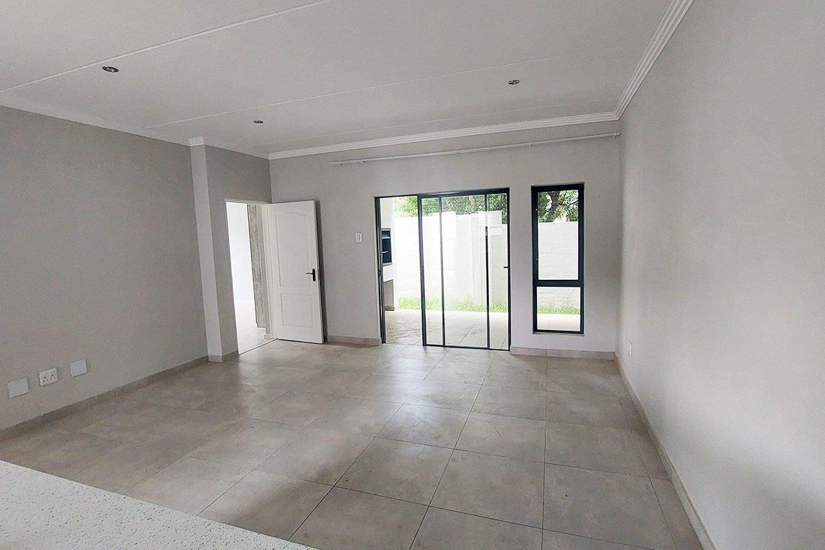 A bright, empty living area featuring neutral tiled flooring, modern aluminium-framed windows, and a sliding door providing access to the outdoor space.