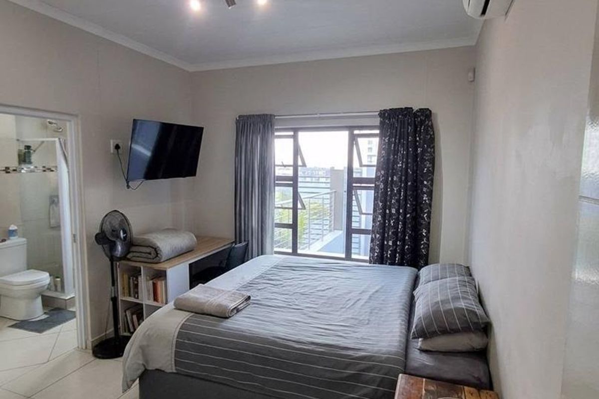 A functional bedroom featuring tiled flooring, a wall-mounted air conditioning unit, and an en-suite bathroom access.