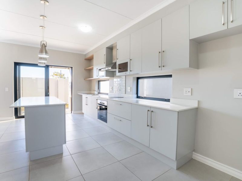 Modern kitchen featuring light grey cabinetry, a central island, quartz countertops, built-in appliances, and direct access to an outdoor patio area.