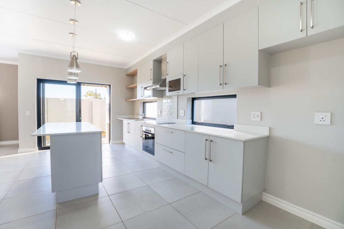 Modern kitchen featuring light grey cabinetry, a central island, quartz countertops, built-in appliances, and direct access to an outdoor patio area.