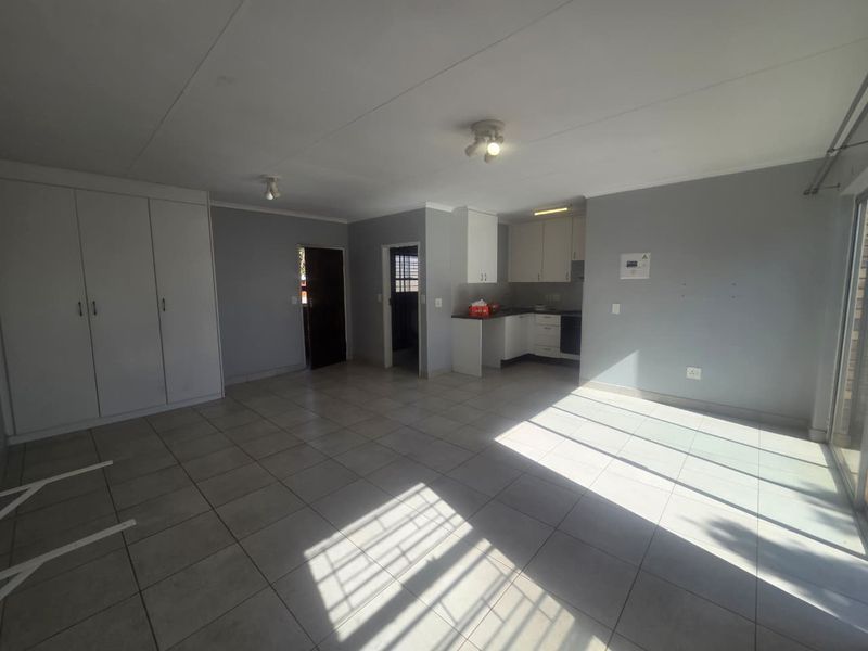 Spacious open-plan living area featuring tiled floors, built-in cupboards, and a functional kitchen layout with neutral finishes.
