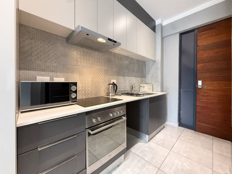 Modern kitchen featuring sleek grey and white cabinetry, integrated oven and hob, patterned tiled backsplash, and high-quality finishes throughout.