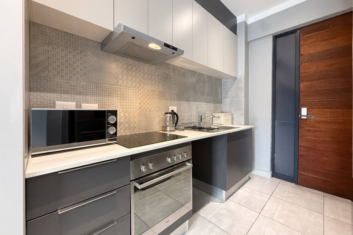 Modern kitchen featuring sleek grey and white cabinetry, integrated oven and hob, patterned tiled backsplash, and high-quality finishes throughout.
