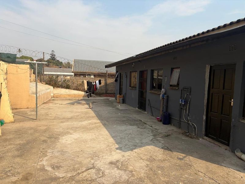 Rear exterior view of the property featuring a concrete paved yard, security fencing, and external access points to the main building structure.