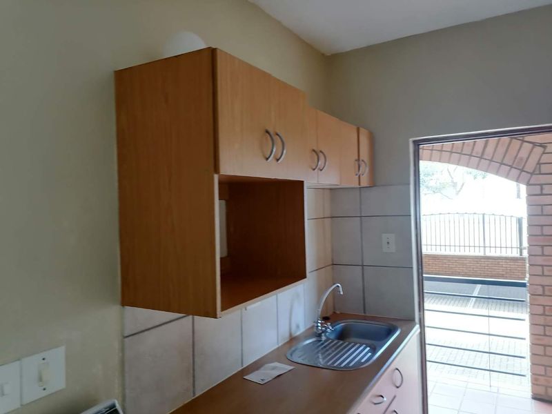 A compact kitchen area featuring laminate cabinetry, a stainless steel sink with mixer tap, and tiled backsplash, providing a functional prep space.