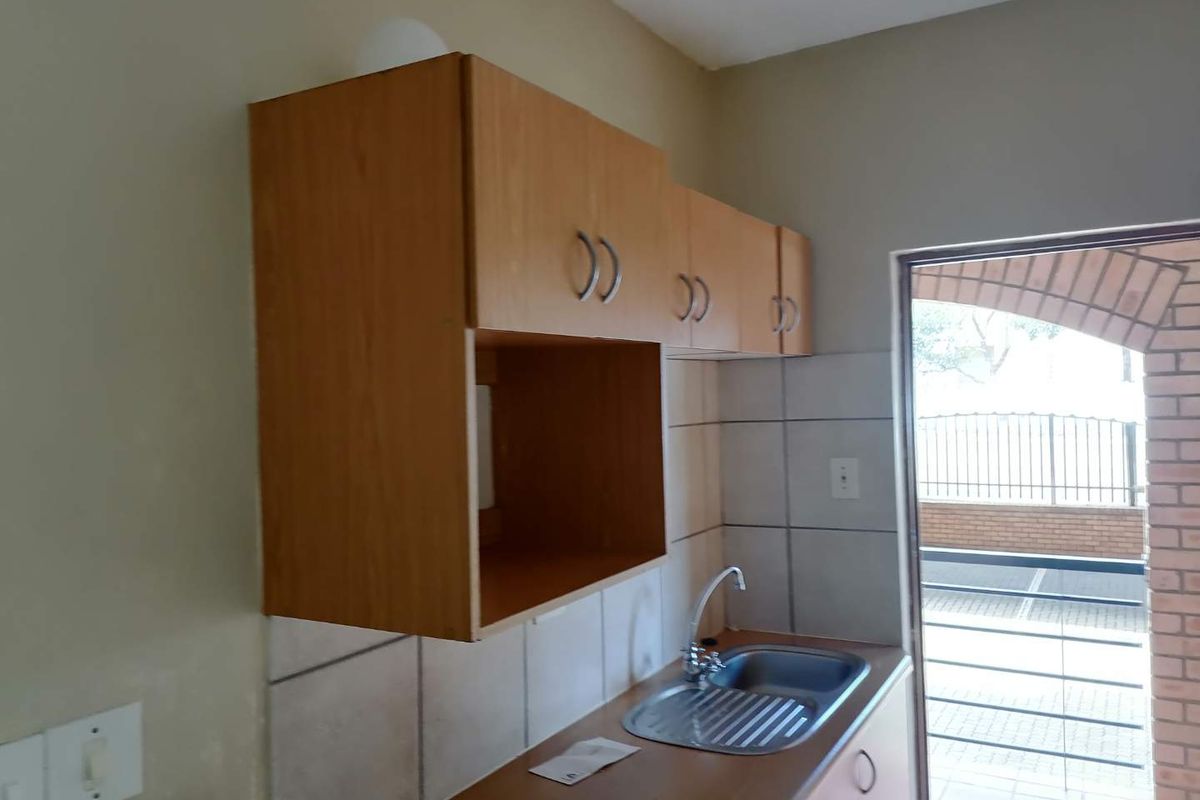 A compact kitchen area featuring laminate cabinetry, a stainless steel sink with mixer tap, and tiled backsplash, providing a functional prep space.