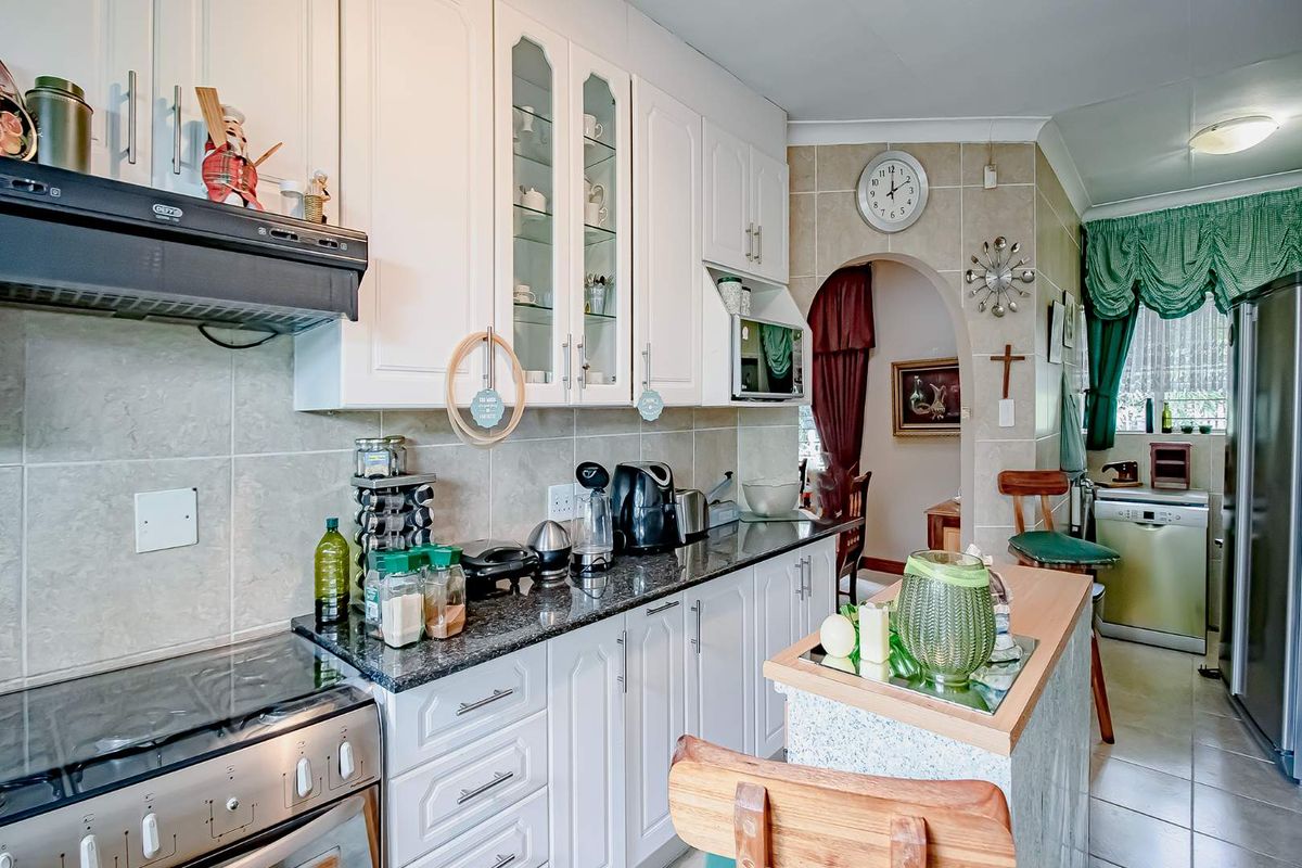 A functional kitchen featuring white cabinetry, granite countertops, a built-in extractor fan, and a breakfast bar, leading through an arched doorway to adjacent living areas.