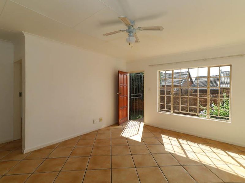 A bright, empty living room featuring tiled flooring, a ceiling fan, and a security gate leading to the exterior.