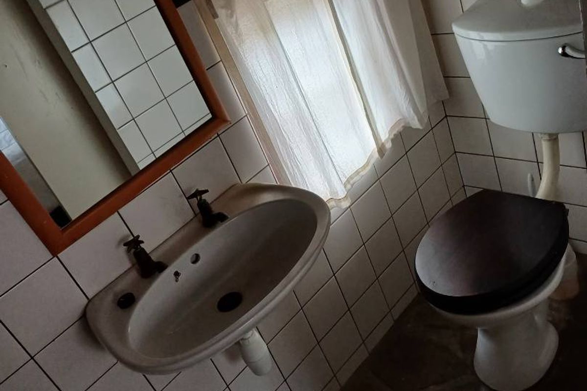 A compact bathroom featuring a wall-mounted basin, a standard toilet, and tiled walls with a rustic stone-style floor.