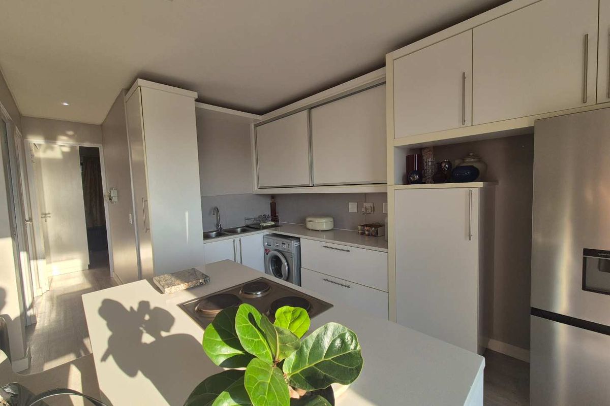 Modern kitchen featuring white cabinetry, a central island with a built-in electric hob, integrated sink, and space for a washing machine.