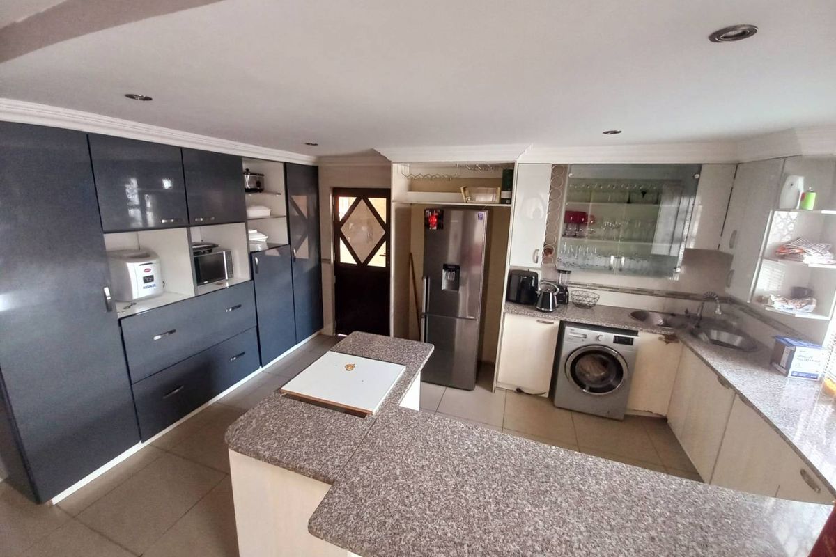 Modern kitchen featuring dark grey cabinetry, granite countertops, a breakfast bar, integrated storage, and a dedicated laundry area with built-in washing machine plumbing.