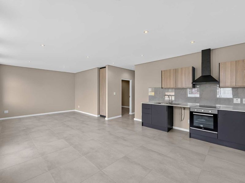 Modern open-plan living area featuring a sleek kitchen with built-in oven, extractor fan, and contemporary cabinetry, finished with neutral tones and large floor tiles.