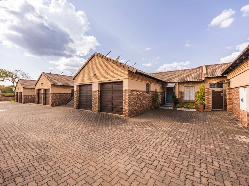 Front exterior view of a townhouse complex featuring brick facades, tiled roofs, and a spacious paved driveway with multiple garage access points.