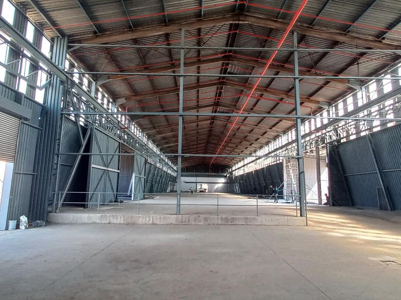 Spacious industrial warehouse featuring a high-clearance steel portal frame, concrete flooring, fire sprinkler system, and large roller shutter access.