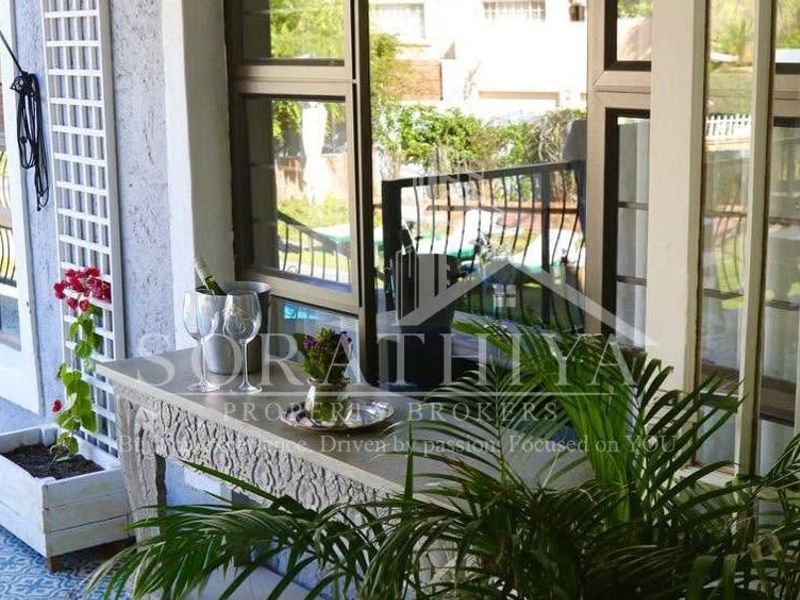 A covered patio area featuring patterned floor tiles, aluminium window frames, and a metal balustrade overlooking the garden.
