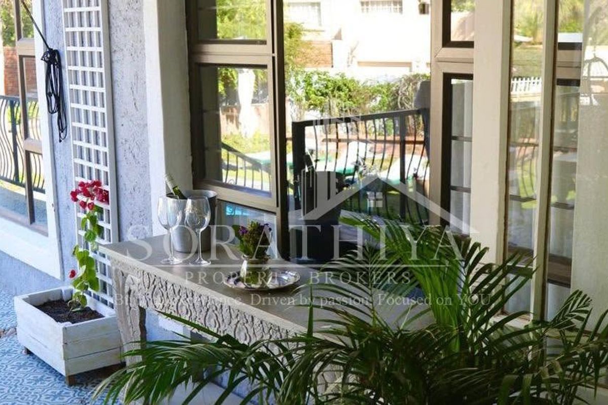 A covered patio area featuring patterned floor tiles, aluminium window frames, and a metal balustrade overlooking the garden.