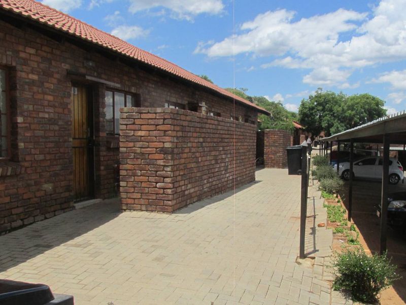 Exterior view of a face brick apartment unit featuring a tiled roof, private entrance area, and adjacent covered carport parking.