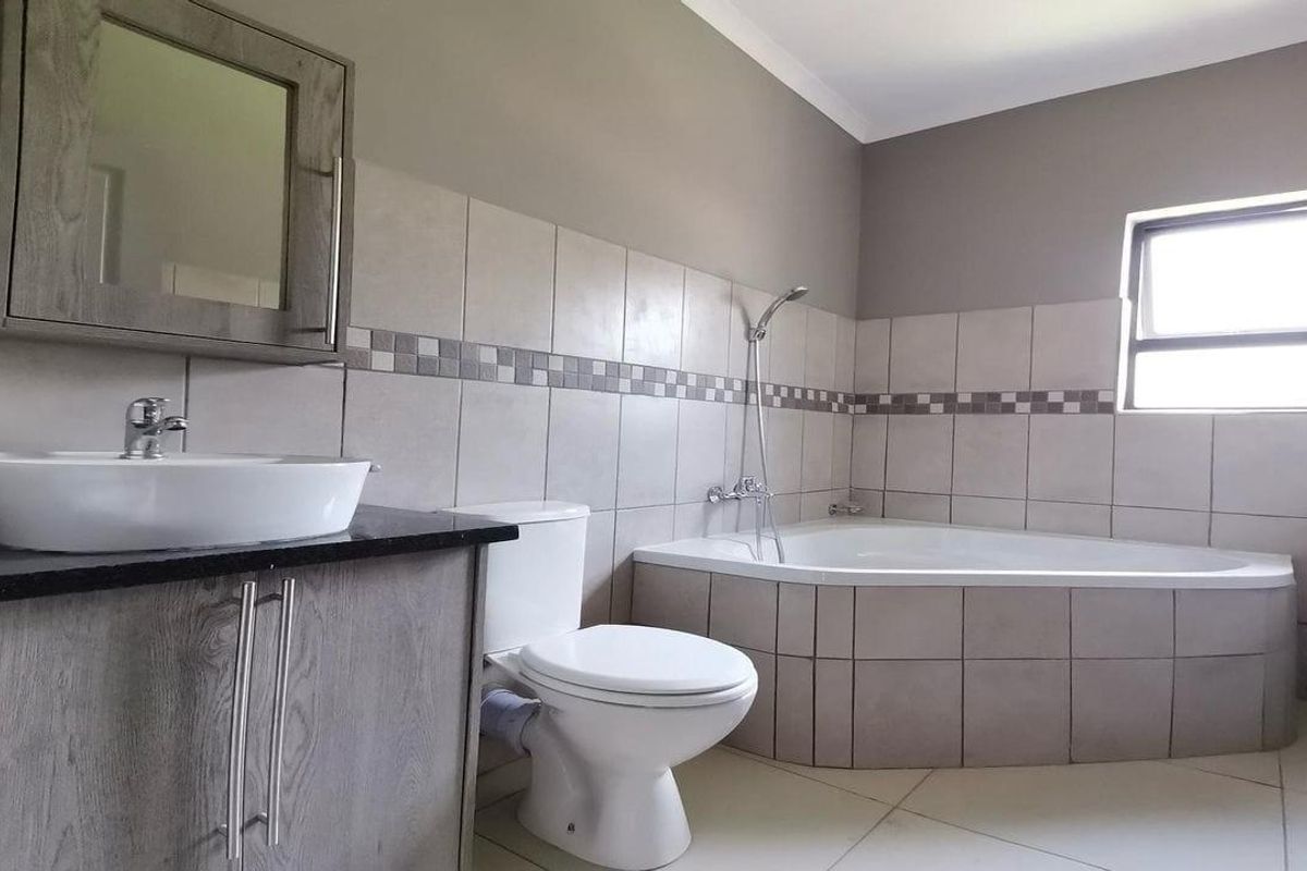 A clean bathroom featuring a corner bathtub, vessel sink with vanity cabinet, and neutral wall tiling.
